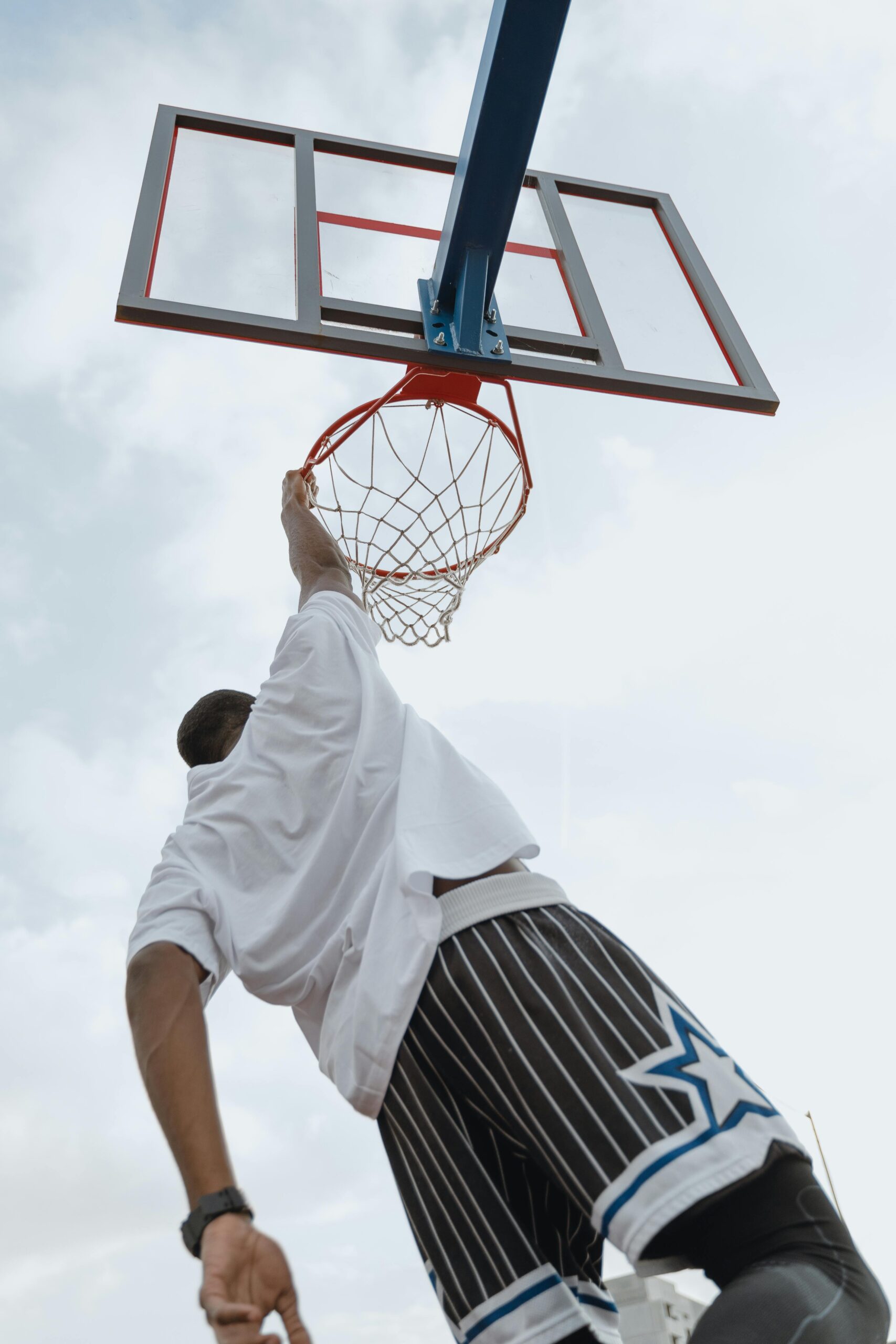 Low-angle shot of a man performing a basketball dunk outdoors with a dramatic sky backdrop.